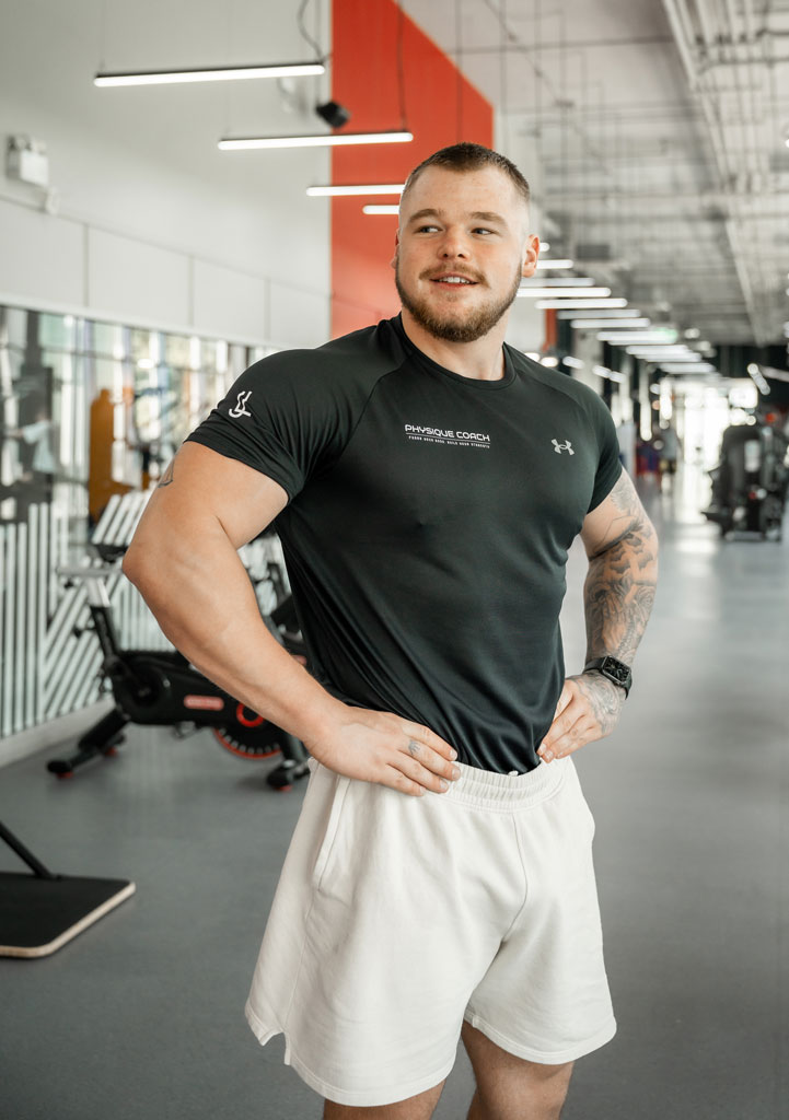 Coach sitting on the floor next to a barbell in the gym, looking away.